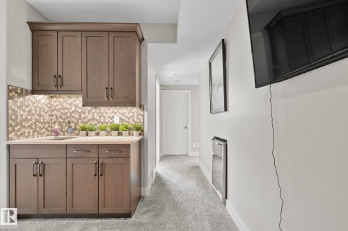 Built-in wet bar featuring wood-finish cabinetry, a hexagonal tile backsplash, light-toned countertop, and undermount sink - 67 Enchanted Way N, St. Albert, AB - Indoor Photo Showing Other Room