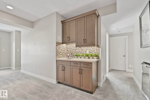 Built-in wet bar featuring upper and lower cabinetry, a light-toned countertop, and a geometric tile backsplash - 67 Enchanted Way N, St. Albert, AB - Indoor Photo Showing Other Room