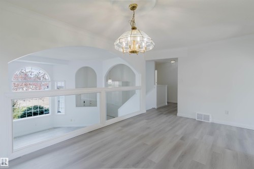 Spacious interior featuring light wood-finish flooring, a decorative chandelier with a ceiling medallion, and arched architectural openings - 13755 131B Avenue, Edmonton, AB - Indoor Photo Showing Other Room