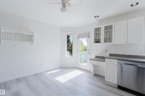 Kitchen area featuring white cabinetry with some glass-front doors, a stainless steel dishwasher, and a speckled countertop - 13755 131B Avenue, Edmonton, AB - Indoor