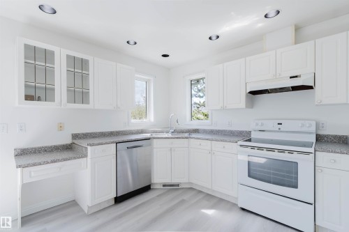 Kitchen featuring white cabinetry, light-toned countertops, stainless steel dishwasher, white electric range, and wood-finish flooring - 13755 131B Avenue, Edmonton, AB - Indoor Photo Showing Kitchen
