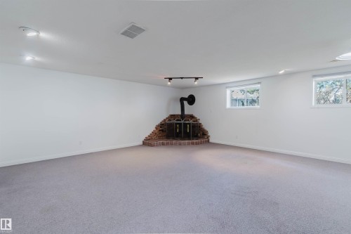 Spacious room featuring light gray carpeting, crisp white walls, multiple windows providing natural light, recessed lighting, and a corner brick-base stove - 13755 131B Avenue, Edmonton, AB - Indoor