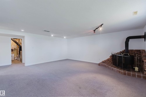 Spacious room featuring light-toned carpeting and a brick-surrounded wood-burning stove with a black stovepipe - 13755 131B Avenue, Edmonton, AB - Indoor Photo Showing Other Room