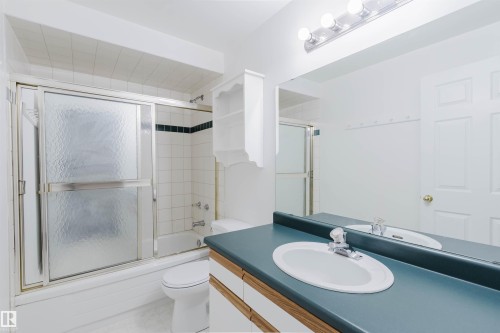 Bathroom featuring a full-width mirror, light wood-finish vanity with dual sinks, and a tub/shower combination with sliding frosted glass doors - 13755 131B Avenue, Edmonton, AB - Indoor Photo Showing Bathroom