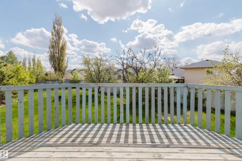 Spacious outdoor deck with a wooden railing and decking, overlooking a landscaped backyard with lush green grass and mature trees - 13755 131B Avenue, Edmonton, AB - Outdoor