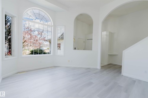 Bright interior space featuring a large arched window, additional tall windows, light wood-finish flooring, and white walls - 13755 131B Avenue, Edmonton, AB - Indoor Photo Showing Other Room