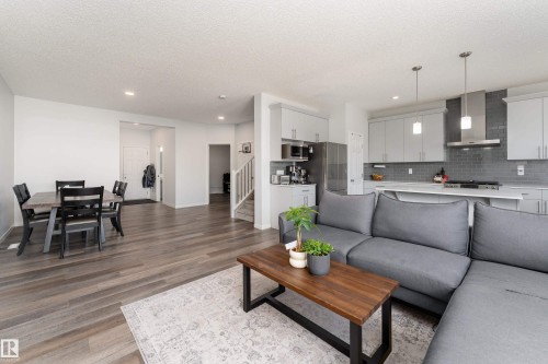 Open-concept living space featuring wood-finish flooring, a modern kitchen with light grey cabinetry, stainless steel appliances, and a grey subway tile backsplash - 5323 Lark Landing Landing, Edmonton, AB - Indoor Photo Showing Living Room
