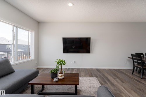 Open-concept living area featuring light gray walls, wood-finish flooring, and a large window - 5323 Lark Landing Landing, Edmonton, AB - Indoor Photo Showing Living Room