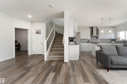 Open-concept living space with wood-finish flooring, a contemporary kitchen, and a carpeted staircase with white railings - 5323 Lark Landing Landing, Edmonton, AB - Indoor Photo Showing Other Room