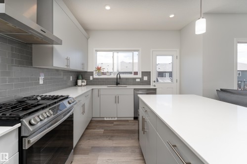 Modern kitchen featuring light gray cabinetry, stainless steel appliances, a subway tile backsplash, and a large central island with a white countertop - 5323 Lark Landing Landing, Edmonton, AB - Indoor Photo Showing Kitchen With Upgraded Kitchen