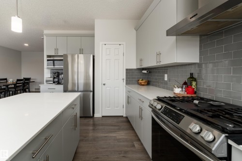 Modern kitchen featuring a white countertop island, stainless steel appliances, grey subway tile backsplash, light grey cabinetry, and wood-finish flooring - 5323 Lark Landing Landing, Edmonton, AB - Indoor Photo Showing Kitchen With Upgraded Kitchen