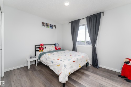 Well-lit room featuring wood-finish flooring, white walls, and a window with dark curtains - 5323 Lark Landing Landing, Edmonton, AB - Indoor Photo Showing Bedroom