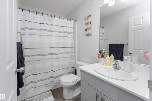 Modern bathroom featuring a single vanity with an integrated sink, a large wall-mounted mirror, overhead lighting, and wood-finish flooring - 5323 Lark Landing Landing, Edmonton, AB - Indoor Photo Showing Bathroom