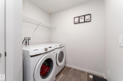 Dedicated laundry area featuring a front-loading washer and dryer, wood-finish flooring, a wire shelf, and neutral wall tones - 5323 Lark Landing Landing, Edmonton, AB - Indoor Photo Showing Laundry Room