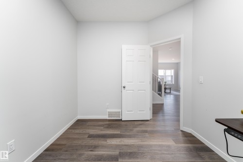 Versatile room with wood-finish flooring, white baseboards, and a paneled door - 5323 Lark Landing Landing, Edmonton, AB - Indoor Photo Showing Other Room