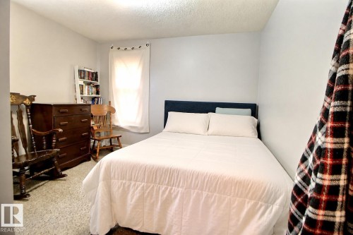 Bright bedroom space featuring a window with white curtains, light-colored walls, and textured carpeting - 11626 87 Street, Edmonton, AB - Indoor Photo Showing Bedroom