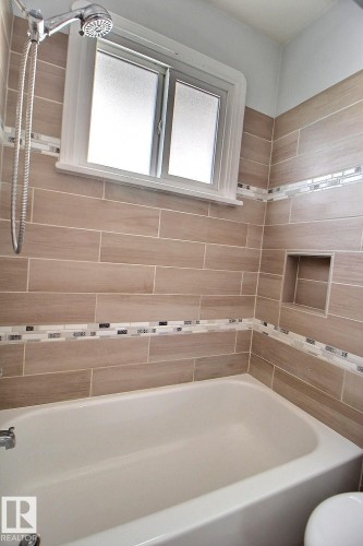Bathtub with wall-mounted showerhead, wood-look tile surround, decorative mosaic tile accents, and an integrated shower niche - 11626 87 Street Nw, Edmonton, AB - Indoor Photo Showing Bathroom