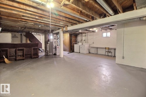 Open basement area with painted concrete flooring, exposed wood beam ceiling, and a built-in wooden bar - 11626 87 Street Nw, Edmonton, AB - Indoor Photo Showing Basement