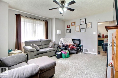 Carpeted living area featuring a ceiling fan with light fixture, window with drapes, and a doorway to an additional room - 11626 87 Street, Edmonton, AB - Indoor Photo Showing Living Room