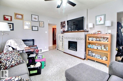 Interior living area featuring a central fireplace with light-toned tile surround and a patterned accent band - 11626 87 Street, Edmonton, AB - Indoor Photo Showing Living Room With Fireplace