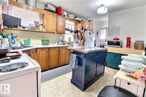 Kitchen featuring wood cabinetry, solid surface countertops, tile flooring, and a central island with a metal countertop - 11626 87 Street, Edmonton, AB - Indoor Photo Showing Kitchen