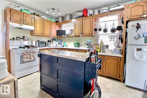 Functional kitchen featuring wood-finish cabinetry, white appliances, and a mobile island with a stainless steel countertop - 11626 87 Street, Edmonton, AB - Indoor Photo Showing Kitchen