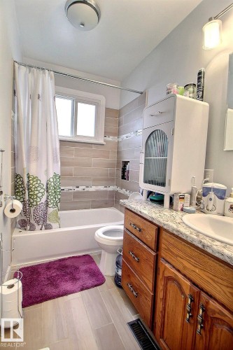 Full bathroom featuring wood-finish tile flooring, a built-in tub with tile surround, a window, and a vanity with a countertop sink - 11626 87 Street, Edmonton, AB - Indoor Photo Showing Bathroom