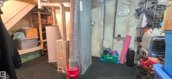 Basement utility area featuring a furnace, hot water heater, and exposed overhead ductwork - 