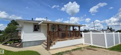 White siding exterior featuring a covered front porch with natural wood railings, stairs, and support beams - 