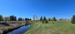 Natural water feature bordered by green spaces, mature trees, and a distant pedestrian bridge - 