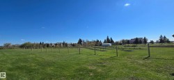 Expansive green space featuring a clear sky, distant trees, and a series of perimeter posts - 