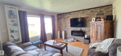 Living area featuring a stone veneer accent wall with a wall-mounted electric fireplace, light wood-finish flooring, and multiple windows - 