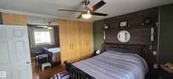 Bedroom featuring a wood-finish accent wall with shelving, a ceiling fan with integrated lighting, wood-finish flooring, and built-in mirrored closet doors with additional wood-finish cabinetry - 