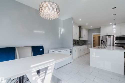 Open-concept kitchen and dining area featuring white cabinetry, stainless steel appliances, a kitchen island with sink, a decorative chandelier, and light-toned tile flooring - 17030 62 Street, Edmonton, AB - Indoor Photo Showing Kitchen With Upgraded Kitchen