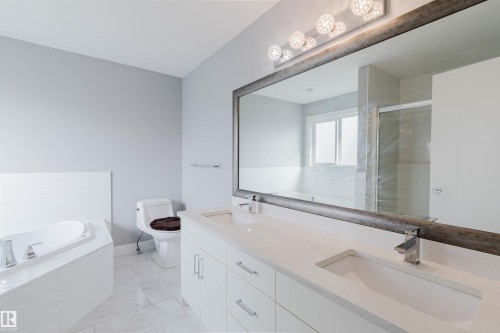 Spacious bathroom featuring a dual vanity with white cabinetry and quartz countertops, an oversized framed mirror, a built-in soaking tub, and a separate glass-enclosed shower - 17030 62 Street, Edmonton, AB - Indoor Photo Showing Bathroom