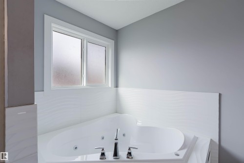 Corner jetted tub with chrome fixtures, surrounded by white tile and a frosted window - 17030 62 Street, Edmonton, AB - Indoor Photo Showing Bathroom