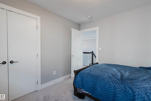 Carpeted room featuring light gray walls, white trim, two white bi-fold doors with black hardware, and an open doorway revealing a dark wood and metal railing - 17030 62 Street, Edmonton, AB - Indoor Photo Showing Bedroom
