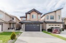 Contemporary stucco exterior featuring a dark asphalt shingle roof, integrated double garage, stacked stone accents, and multiple front-facing windows - 17030 62 Street, Edmonton, AB  - Outdoor With Facade 