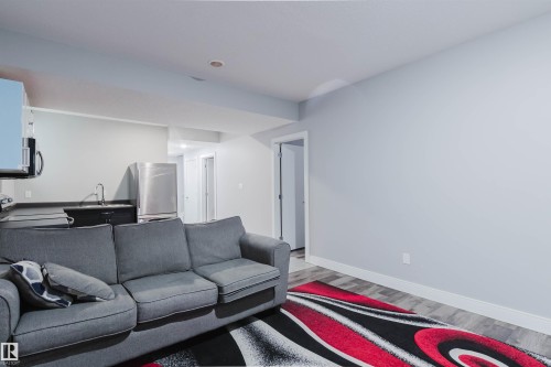 Open-concept living space with light gray walls, recessed lighting, wood-finish flooring, and a compact kitchenette featuring a stainless steel refrigerator and sink - 17030 62 Street, Edmonton, AB - Indoor Photo Showing Living Room