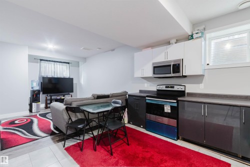 Recessed lighting illuminates this open-concept space featuring a compact kitchen area with white upper cabinetry, grey lower cabinetry, and a built-in microwave - 17030 62 Street, Edmonton, AB - Indoor Photo Showing Kitchen