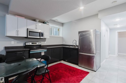 Modern kitchen featuring stainless steel appliances, white upper cabinetry, and dark lower cabinetry with coordinating countertops - 17030 62 Street, Edmonton, AB - Indoor Photo Showing Kitchen