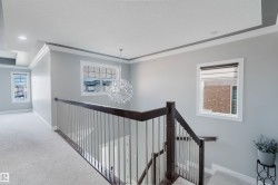 Upper-level landing featuring a contemporary chandelier, recessed lighting, white trim, dark wood-finish handrail, and light-tone carpeting - 