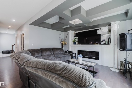 Living area featuring wood-finish flooring, a contemporary tray ceiling with recessed lighting, and a linear electric fireplace with a white mantel and built-in shelving - 17030 62 Street, Edmonton, AB - Indoor Photo Showing Living Room With Fireplace