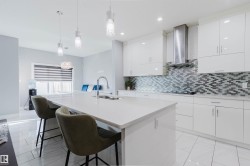 Contemporary kitchen featuring a large center island with integrated sink, white flat-panel cabinetry, a tile backsplash with a mosaic pattern, stainless steel range hood, and white tile flooring - 