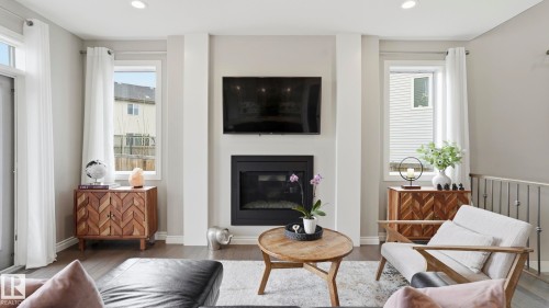 Living area featuring a central fireplace with a mounted television, flanked by two large windows - 2620 Adam Crest, Edmonton, AB - Indoor Photo Showing Living Room With Fireplace