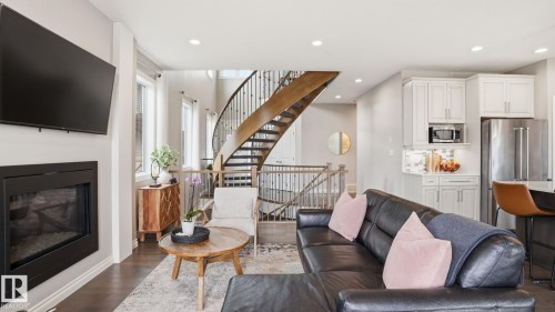Open-concept living area featuring a prominent spiral staircase with dark wood treads and wrought iron balusters - 2620 Adam Crest, Edmonton, AB - Indoor Photo Showing Living Room With Fireplace