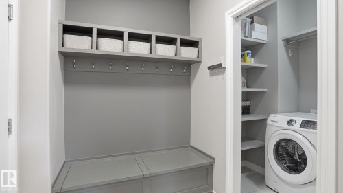 Built-in mudroom bench with cubbies and coat hooks, complemented by a dedicated laundry closet featuring a front-load washer and integrated shelving - 2620 Adam Crest, Edmonton, AB - Indoor Photo Showing Laundry Room