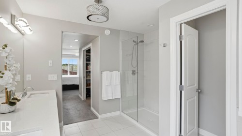 Contemporary bathroom featuring a dual vanity with white countertops and undermount sinks, a glass-enclosed walk-in shower with tile surround, and a decorative ceiling light fixture - 2620 Adam Crest, Edmonton, AB - Indoor Photo Showing Bathroom