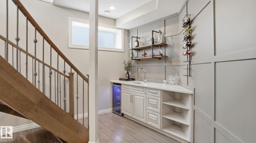 Custom built-in wet bar featuring a beverage cooler, white cabinetry, a sink with a gooseneck faucet, and open shelving - 2620 Adam Crest, Edmonton, AB - Indoor Photo Showing Other Room
