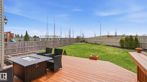 Spacious backyard featuring a large wood-finish deck, expansive lawn, perimeter fencing, and mature plantings - 2620 Adam Crest, Edmonton, AB - Outdoor With Deck Patio Veranda